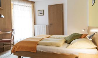 A cozy bedroom with a double bed and colorful pillows. Bright curtains let in plenty of light and there is a small study.