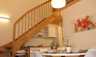 A modern apartment with a wooden staircase and a cozy dining table. A painting with red flowers hangs on the wall.