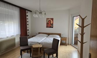 A cozy bedroom with a double bed and two chairs. The walls are light, and there is a picture as well as access to the terrace.