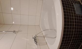 A modern bathtub in a white tiled room. The tub has an elegant round shape and is surrounded by a dark tile border.