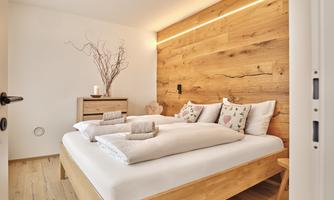 An inviting bedroom with a wooden bed and warm wood paneling. The cozy atmosphere is enhanced by decorative cushions and soft lighting.