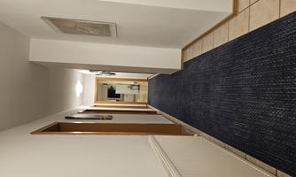 A narrow corridor with light walls and wood frames on the doors. The floor is covered with a blue carpet.