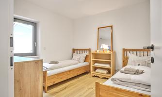 A bright bedroom with two single wooden beds. On a dresser sits a mirror and a lamp.