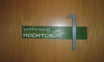 A wooden sign with the inscription "Apartment HOCHTOR" in white letters. The sign is green and has a gray number "1" next to it.