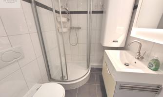 A modern bathroom with a shower cabin, a sink, and a toilet. The walls are tiled in white and the floor is in dark gray.