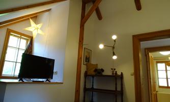 A cozy room with wooden beams, a television, and a beautiful lamp. A window lets in plenty of daylight and creates an inviting atmosphere.