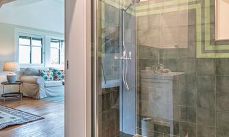 A modern shower with green tiles and clear lines. In the background, a cozy living area is visible.