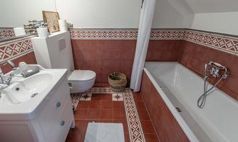 A bathroom with red-checkered tiles and a bathtub. There is a sink, a toilet, and decorative elements on the walls.