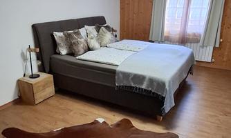 A modern bedroom with a large bed and decorative pillows. The floor is covered with a fur rug and the room has plenty of daylight.