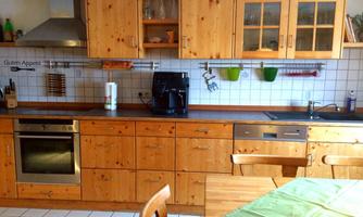 A cozy kitchen with wooden furniture and modern appliances. The table is set with a green tablecloth.
