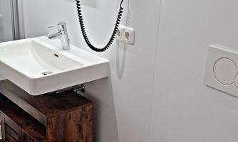A modern bathroom with a sink, a large mirror, and a toilet. A hairdryer is hanging on the wall.