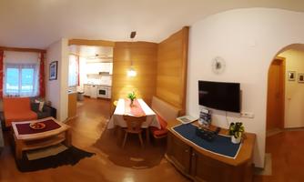 A cozy living room with a seating area, a coffee table, and a television. There is also an open kitchen and a dining area with a table and chairs.