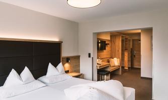 A modern hotel room with two beds and a cozy design. In the background, there is a small living area with a TV and chairs.