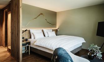 A modern bedroom with a large bed and stylish wooden decor. The walls are painted in soft colors and there is a cozy seating area.