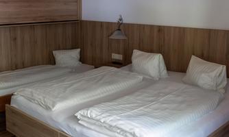 A simple bedroom with two single beds and wooden paneling. There is a bedside lamp and a cozy, minimalist style.