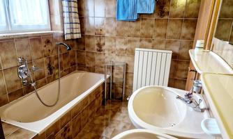 A bathroom with a bathtub and a sink. The walls are tiled with brown tiles, and a towel hangs on the wall.
