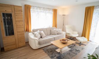 A modern living room with a comfortable sofa and an elegant armchair. Large windows let in plenty of daylight, and the warm color scheme creates an inviting atmosphere.