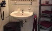 A small bathroom with a sink and a mirror. There are shelves with towels and a hairdryer on the wall.