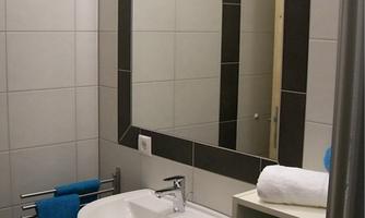 A modern bathroom with a sink and a large mirror. Towels in blue are neatly stored, and the walls are brightly tiled.