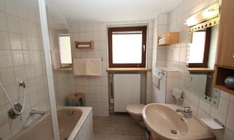 A bright bathroom with a bathtub and a shower. There are windows and modern wooden furnishings.