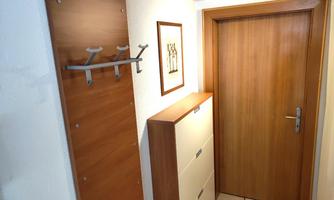 A bright entrance area with a wooden cabinet and a wall holder for jackets. Next to the door is a framed picture.