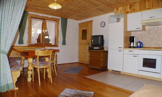A cozy living space with a wooden ceiling, a dining table, and a small kitchen. There are windows with curtains and a television in the room.