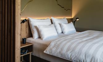 A modern bedroom with a large bed and several pillows. The warm lighting creates a cozy atmosphere.