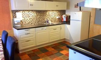 A modern kitchen with white cabinets and colorful tiles. The facilities include a refrigerator, a sink, and a coffee machine.