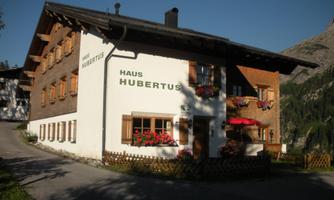A cozy house named "Haus Hubertus" with flower boxes and a red parasol. The building is situated in a picturesque mountain landscape.
