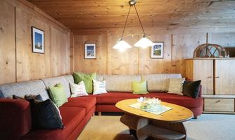 A cozy living room with a red couch and several cushions. The walls are made of wood and there is a rustic wooden dresser as well as some picture frames.