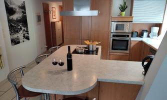 A modern kitchen with wooden cabinets and a bright countertop. On the counter, there are two wine glasses and a pot of spaghetti.