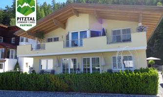 A modern house with a bright facade design and a large balcony. Surrounded by well-maintained trees, it presents itself in a picturesque setting.