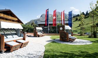 A beautiful outdoor area with loungers and green grass. In the background, flags are fluttering and the mountains are visible.