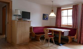 A cozy room with a wooden bench and a table. On the table is a white cloth, and there is a television on the wall.