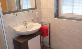 A modern bathroom with a sink, a mirror, and a towel. The floor is tiled and a red towel is lying on the floor.