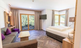 A modern hotel room with a large bed and a cozy seating area. The windows provide a beautiful view of the green landscape.