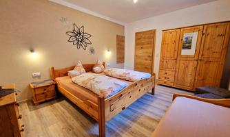 A bright bedroom with two wooden beds and a cozy nightstand. The walls are in neutral colors and there is a large wooden wardrobe.