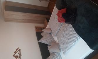 A cozy bedroom with a large bed and checkered pillows. A wardrobe and a small table complement the furnishings.
