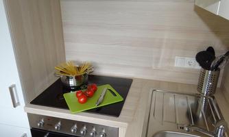 A modern kitchen with a stove and a pot in which spaghetti is cooking. Fresh tomatoes and a knife are on a green cutting board.