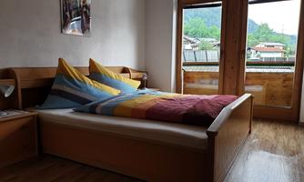 A cozy bedroom with a double bed and colorful pillows. Large windows provide a view of the surroundings.