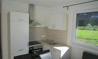 A modern kitchen with white cabinets and a stove. A window provides a view of a green garden.