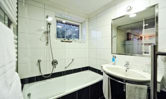 A modern bathroom with a bathtub and shower. The walls are tiled, and there is a sink as well as a mirror.