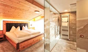 A cozy bedroom with a wooden bed and large pillows. On the right, there is a modern tiled shower with glass partition.