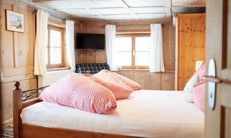 A cozy bedroom with a double bed and checked pillows. Bright windows and wooden paneling create an inviting atmosphere.