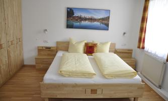 A cozy bedroom with a double bed and yellow bedspreads. The room has wooden furniture and a large window with curtains.