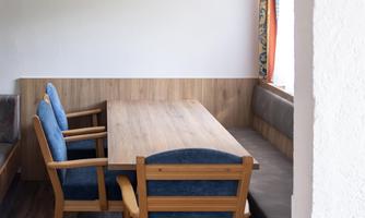 A bright room with a table and cozy chairs. The wall is visible through an arch, and light falls through a window.