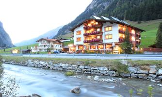 A cozy hotel in the mountains, surrounded by green meadows and rocks. A quiet river flows right next to the building.
