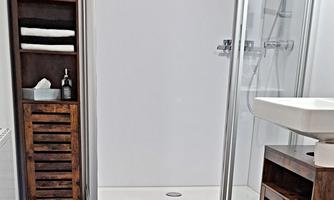 A modern bathroom with a glass shower and a stylish sink. Next to the shower stands a wooden shelf with towels and care products.