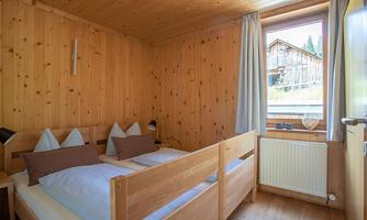 A cozy room with wooden paneling and two beds. There is a window with a view of nature and soft lighting.