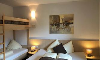 A cozy bedroom with two beds and a loft bed. The walls are painted light, and a painting hangs above the bed.